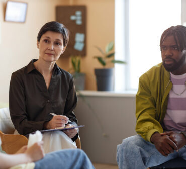 Mature psychologist working with group of people at psycho session in office