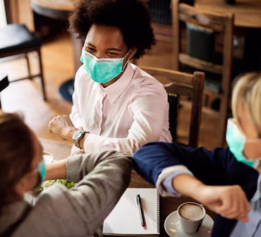 happy-businesswomen-with-face-masks-elbow-bumping-cafe_637285-8144